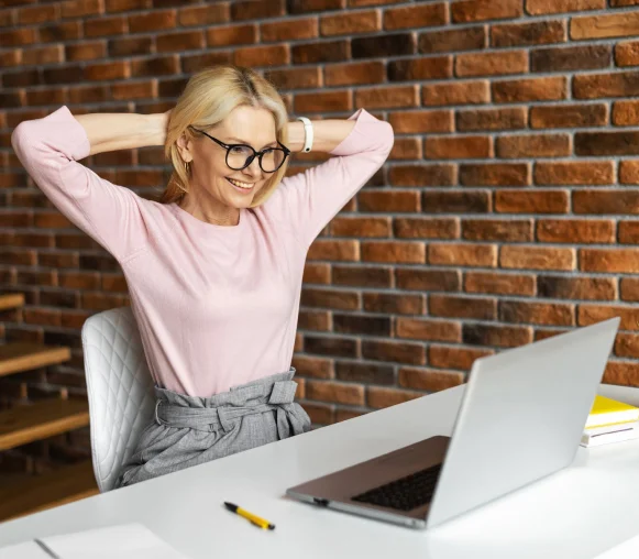A woman at her desk stretching with a relieved smile, free of shoulder tension